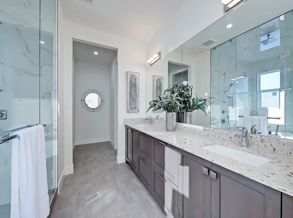 A bright, modern master bathroom featuring a long grey vanity with a white speckled countertop and large vanity mirror.