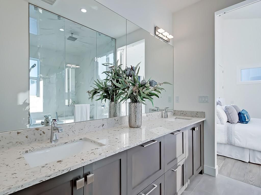 A modern bathroom with a double vanity featuring gray cabinets, a speckled granite countertop, and a large wall mirror.