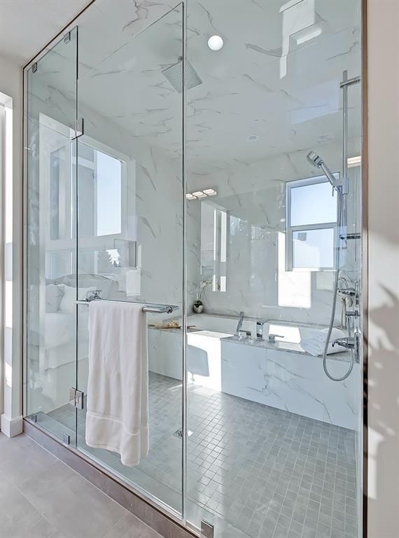A modern glass-enclosed shower with white marble walls and a white towel hanging on the door handle.
