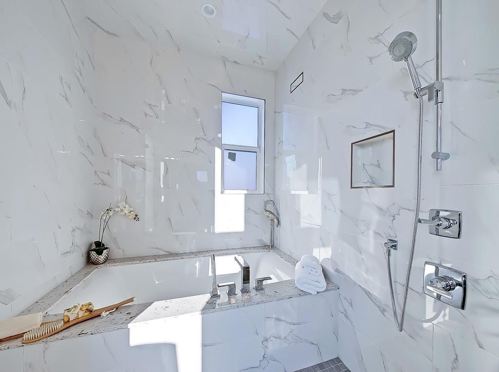 A modern bathroom featuring a white marble bathtub, a separate shower with chrome fixtures, and a small window.