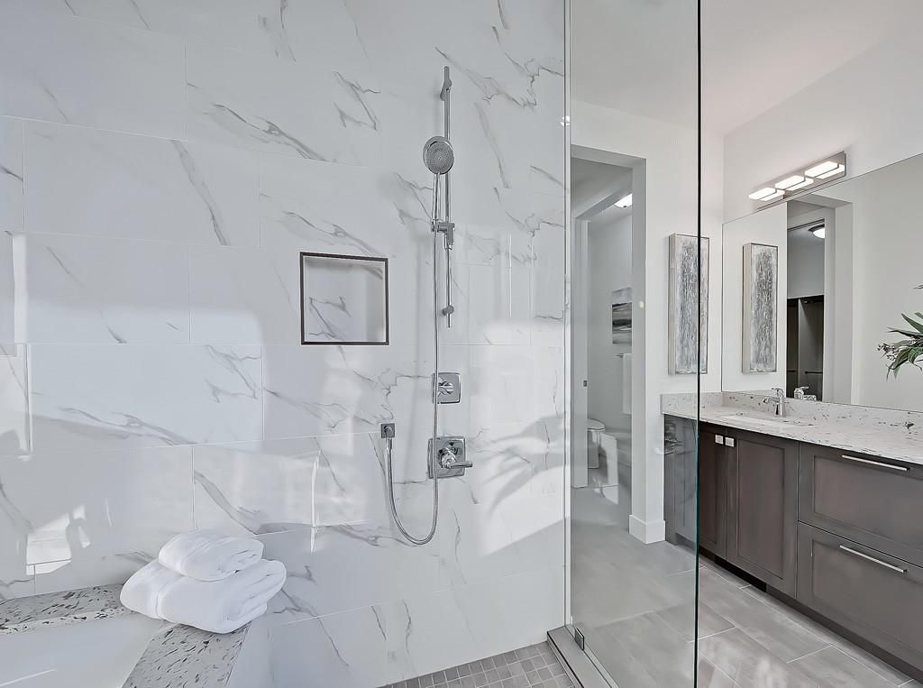 A modern bathroom featuring a glass-enclosed shower with marble-style tile walls next to a dark wood double vanity.