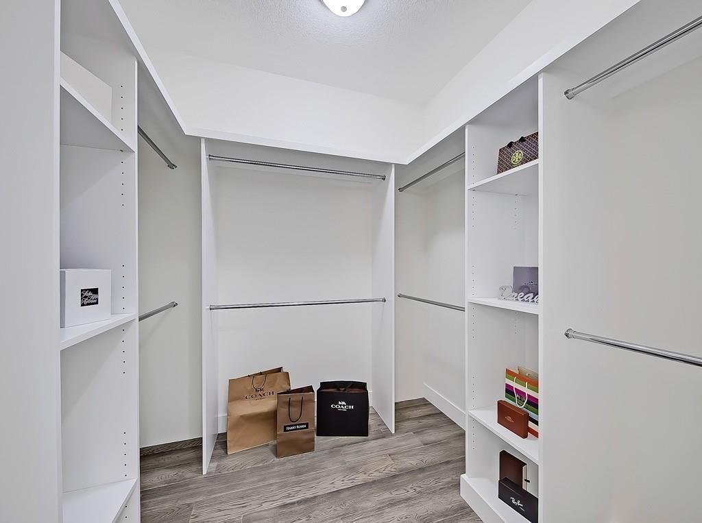 A bright, empty walk-in closet with white shelving units, clothing rods, and several shopping bags on the wood floor.