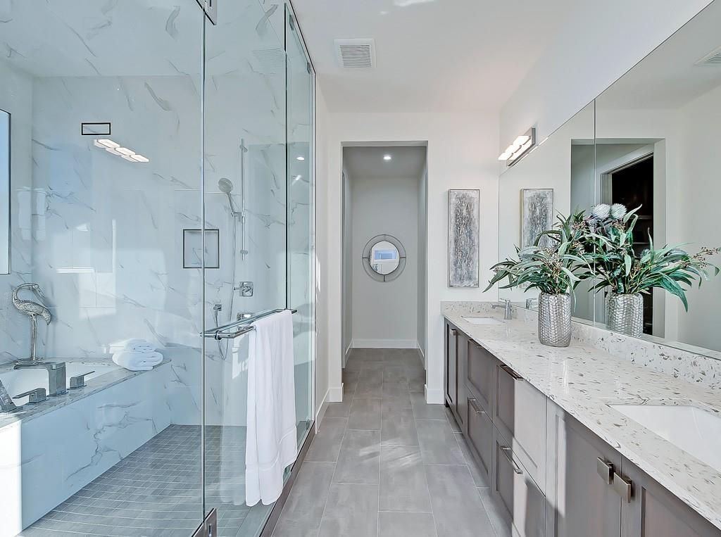 Modern bathroom with marble-style shower, gray vanity, double sinks, and a central entryway leading to another room.