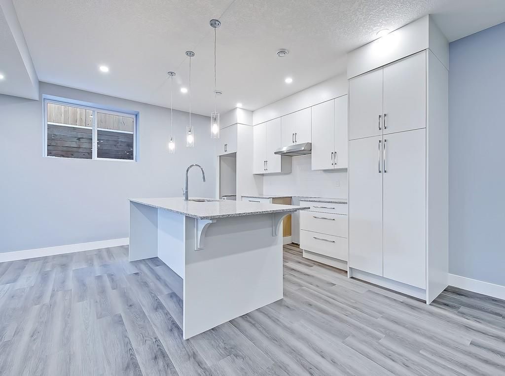 A modern kitchen featuring white cabinets, a large central island with a sink, and grey wood-look flooring.