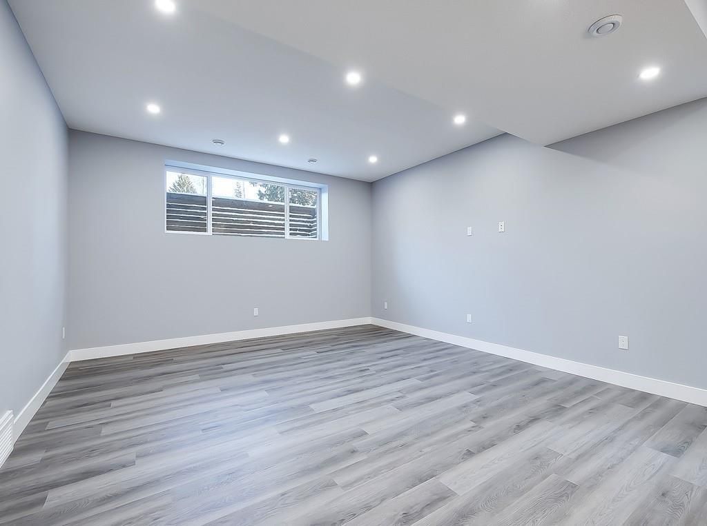 A bright, empty room with light gray walls, white trim, and gray wood-look flooring, featuring a rectangular window.