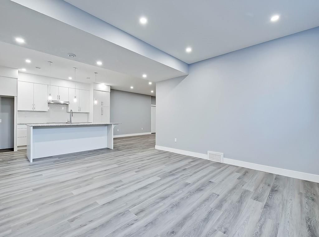A bright, modern room with light gray walls, gray wood-look flooring, recessed lighting, and a white kitchen island.