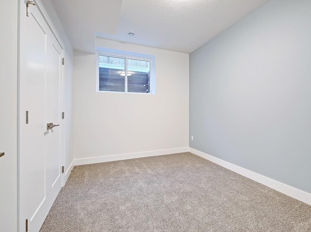 A small, empty bedroom featuring gray carpet, white double doors, a white window, and light blue and white walls.
