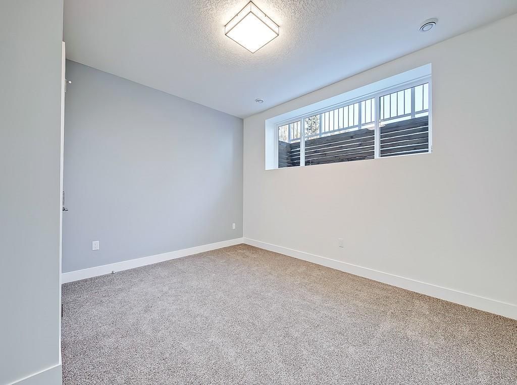 An empty bedroom with light grey walls, carpeted flooring, and a single rectangular window near the ceiling.