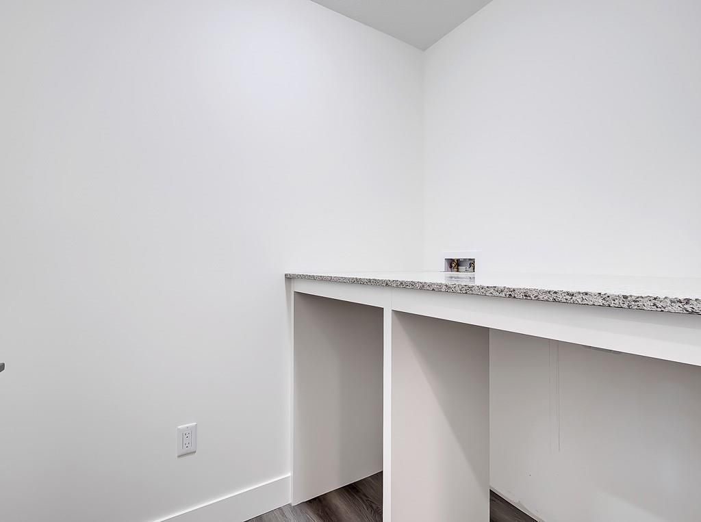 A white alcove featuring a speckled grey granite countertop supported by white dividers over a dark wood-look floor.