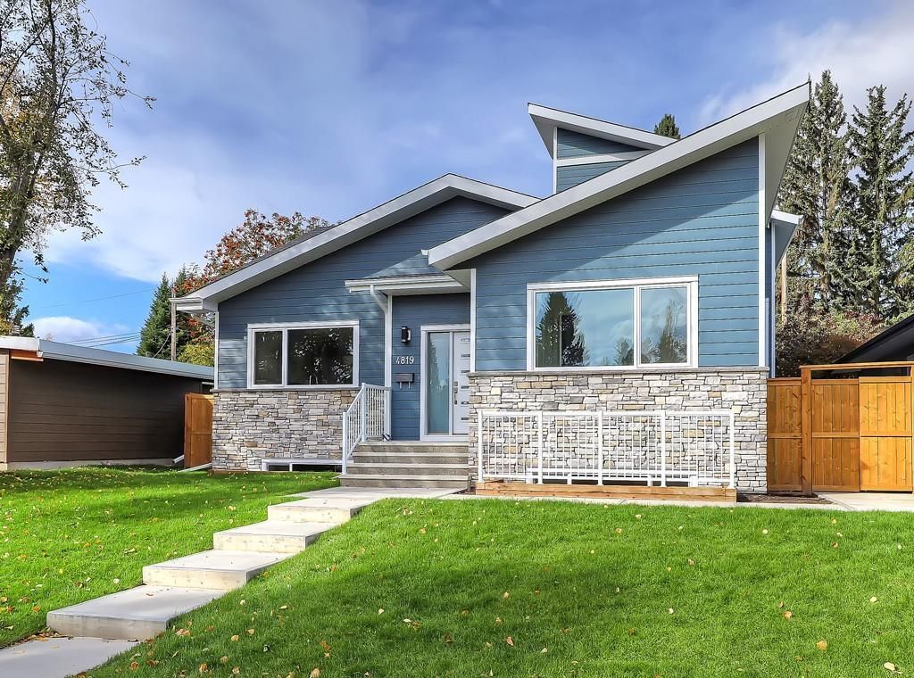 A modern house with blue siding, stone veneer, and angled rooflines, featuring a grassy lawn and a stone walkway.
