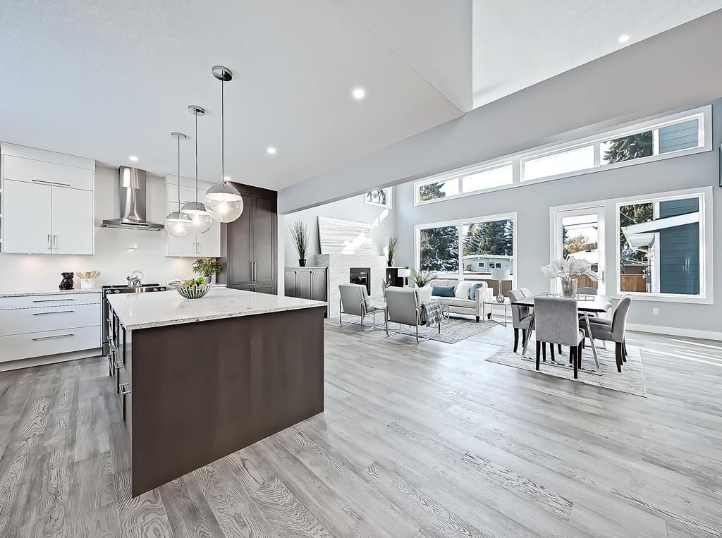A modern open-concept kitchen and living area featuring a large dark kitchen island, white cabinets, and wood flooring.