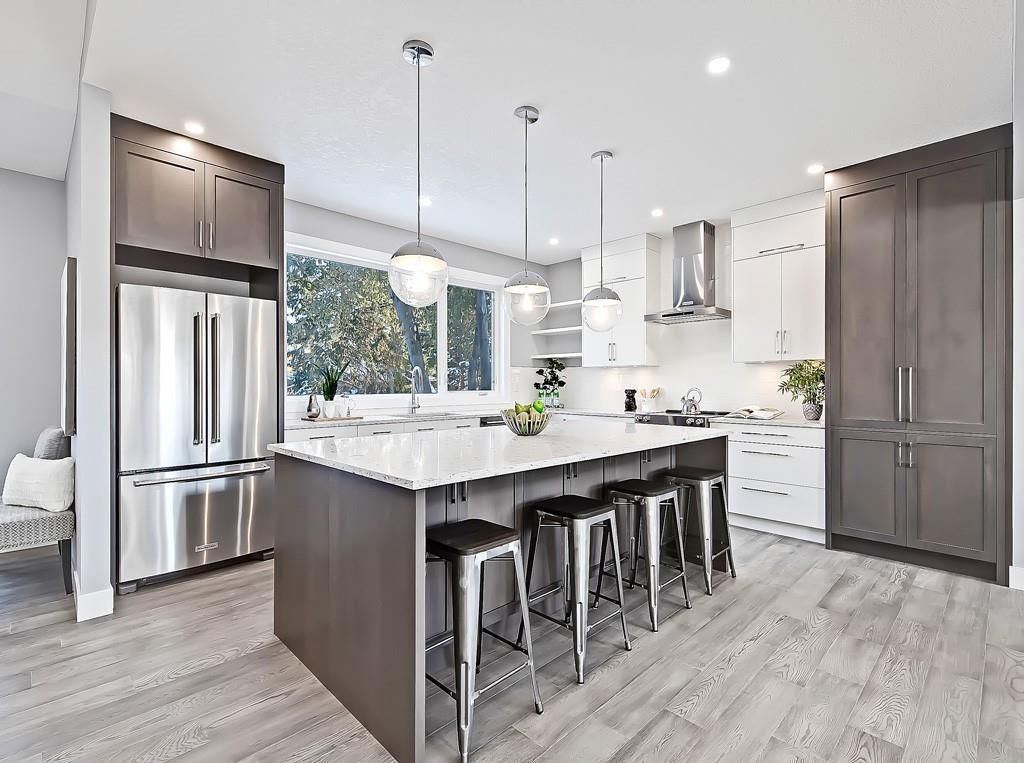 A modern, well-lit kitchen featuring a large central island with bar stools, dark wood cabinetry, and stainless appliances.