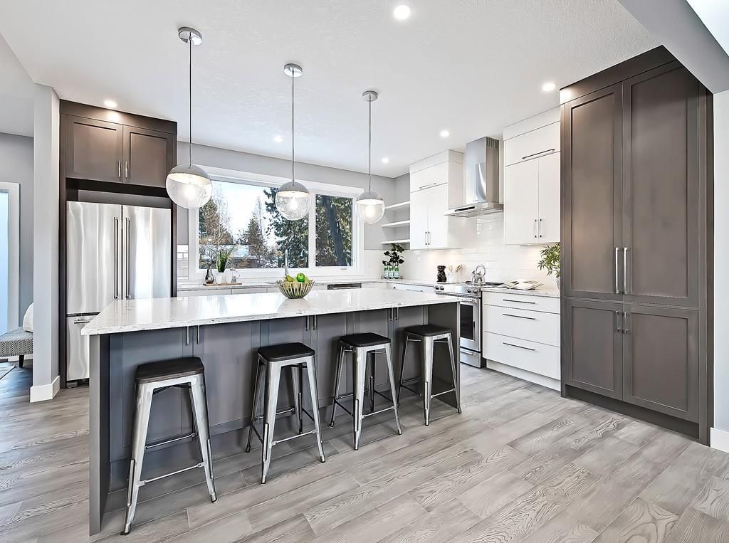 A modern kitchen with a white island, three bar stools, dark grey cabinetry, and white countertops.