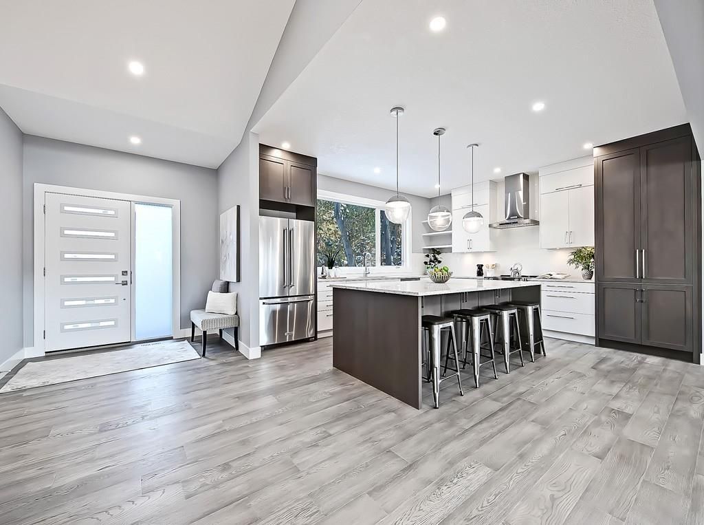 A modern open-plan kitchen with a dark-wood island, bar stools, white cabinetry, stainless appliances, and grey floors.