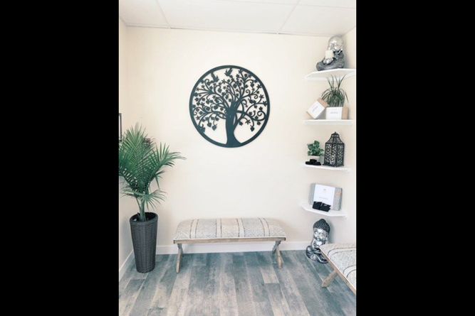 A tranquil waiting area with a central tree wall art, a bench, a potted plant, and shelves with decor on light wood floors.