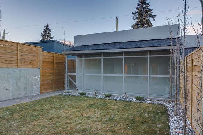 A small backyard with a patch of lawn, a modern glass-enclosed structure, and wooden privacy fences on both sides.