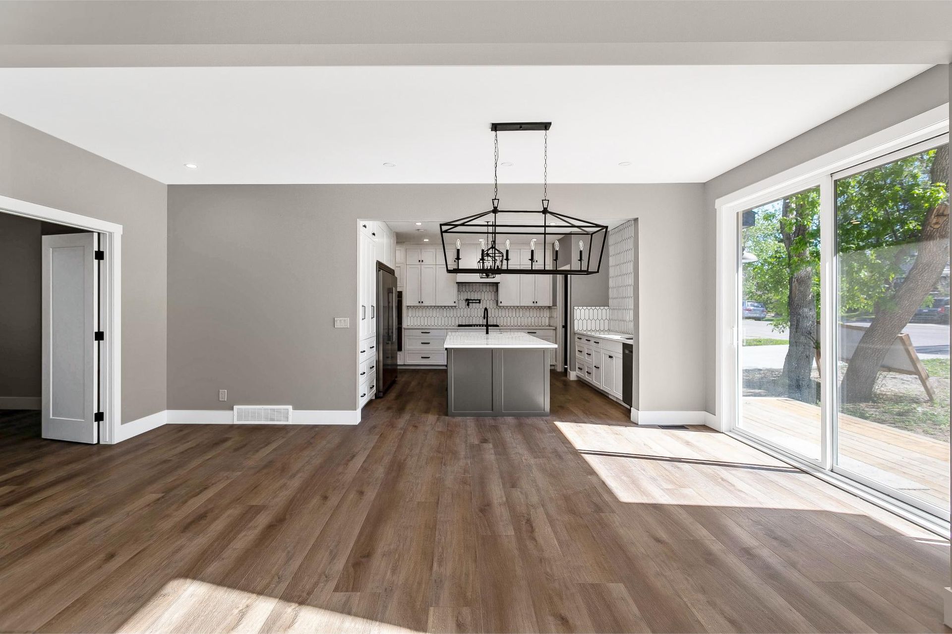An open floor plan with wood flooring, grey walls, a kitchen island, and large glass sliding doors leading to the outside.