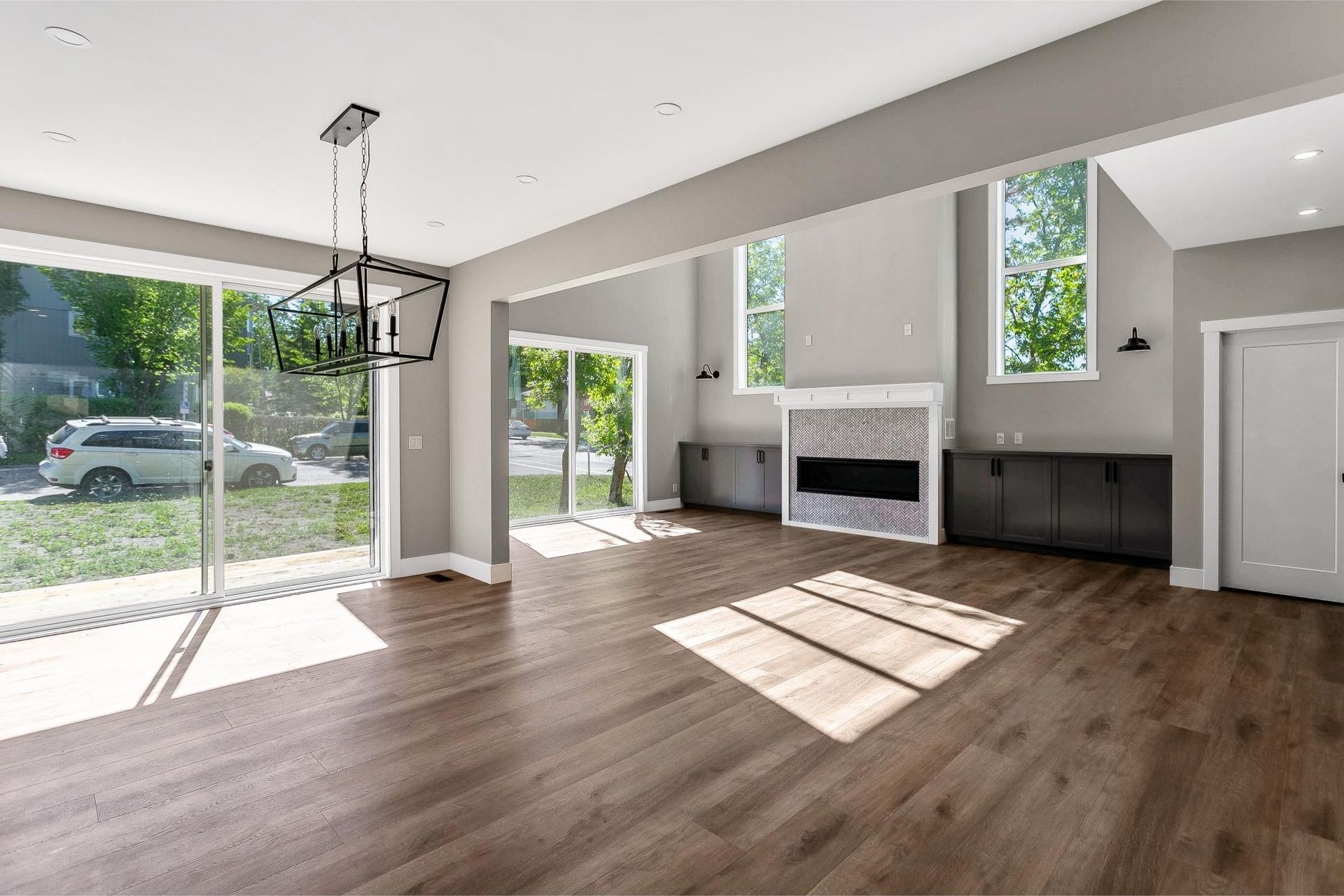 A spacious living area with hardwood floors, a stone fireplace, dark cabinets, sliding glass doors, and a dining light.