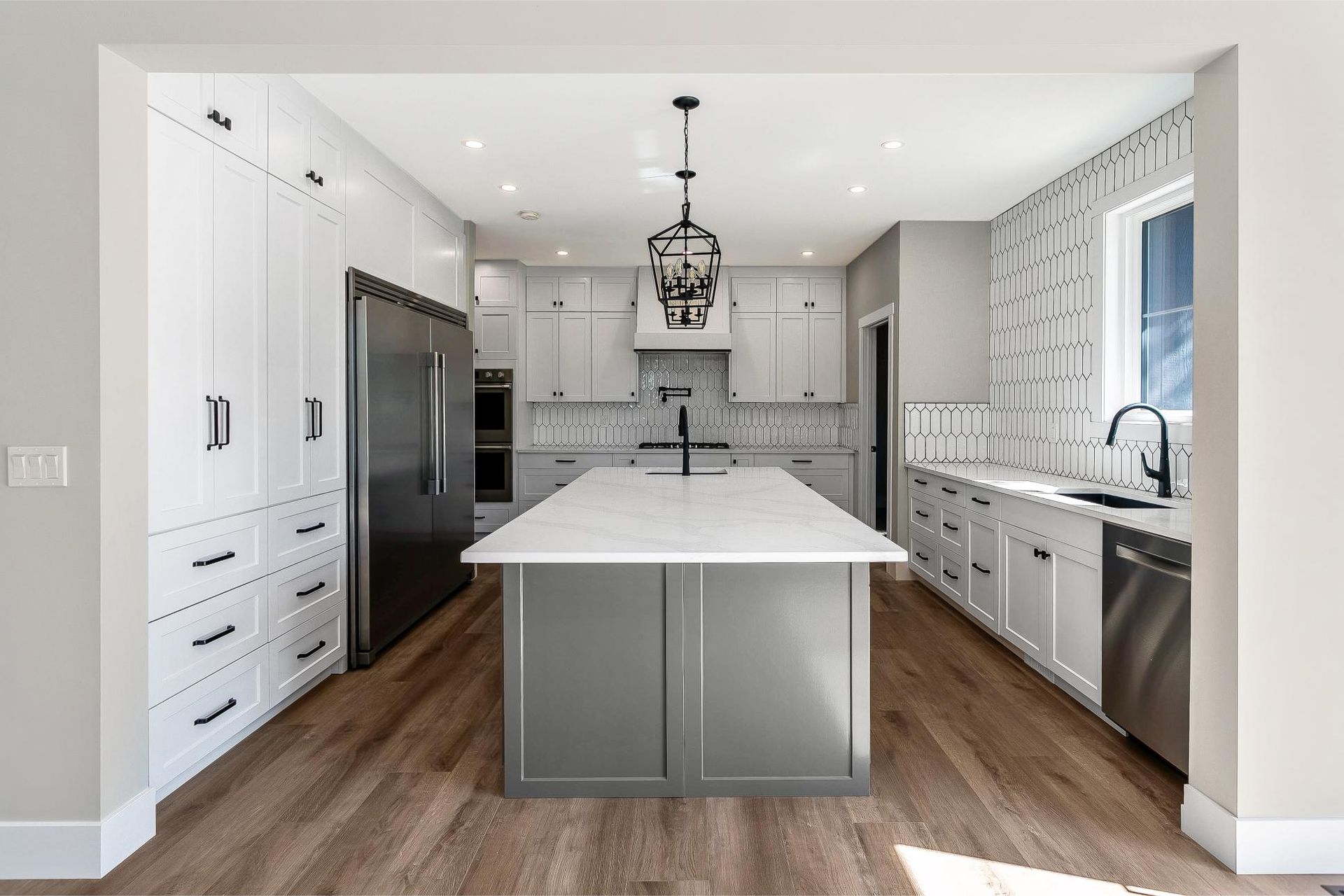 Modern kitchen featuring white cabinets, a dark gray island with white countertop, stainless appliances, and wood floors.