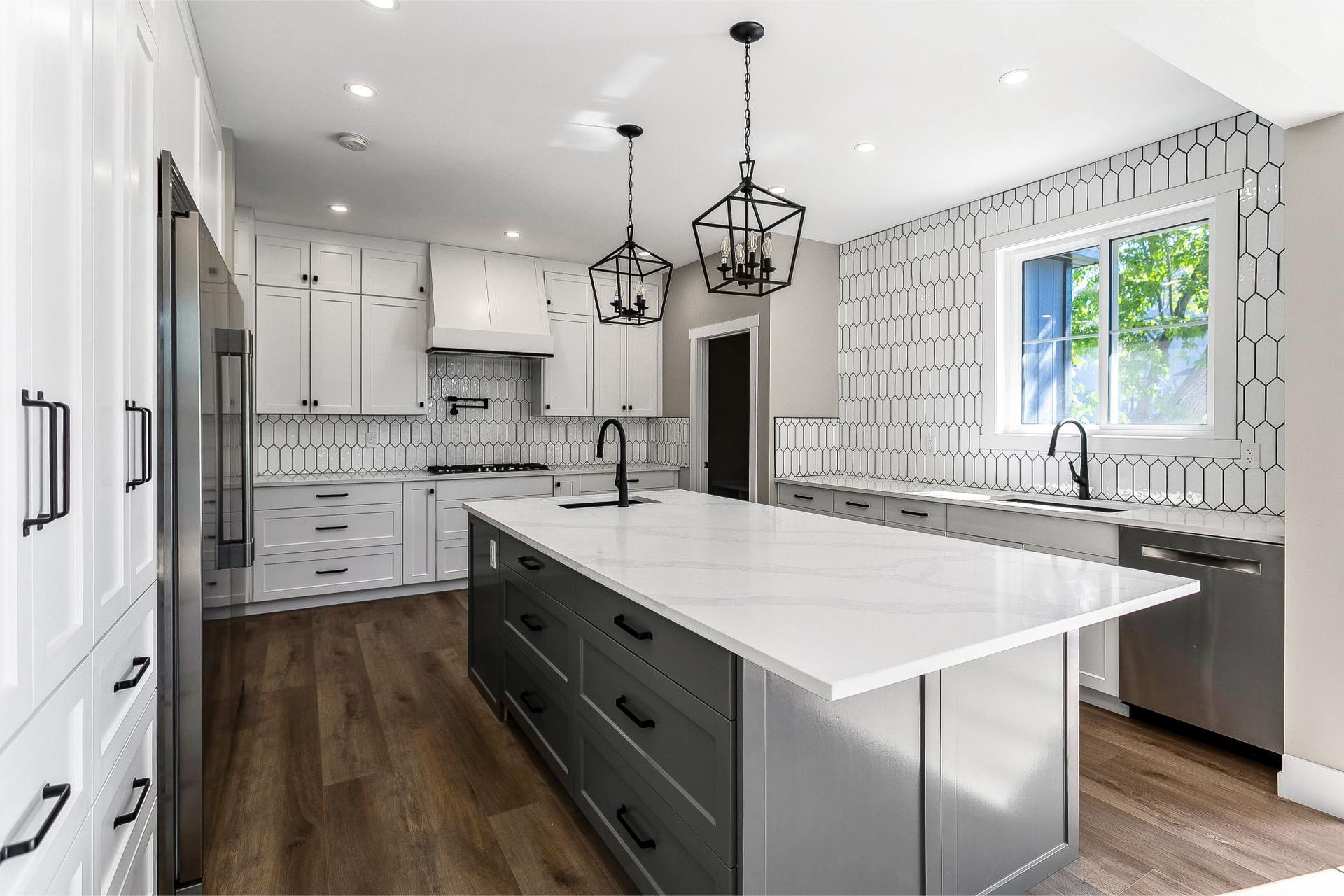 Modern kitchen with a dark grey island, white cabinets, white marble countertops, and geometric backsplash tiles.