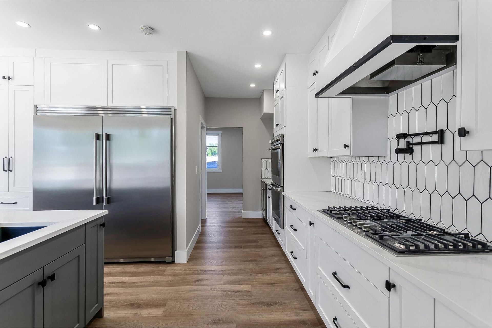 A modern kitchen featuring white cabinets, stainless steel appliances, a gray kitchen island, and white hexagon tile backsplash.