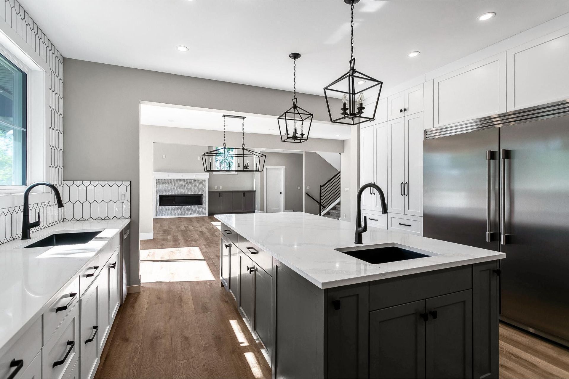 A modern kitchen with dark grey island cabinetry, white quartz countertops, black fixtures, and a view into the living room.