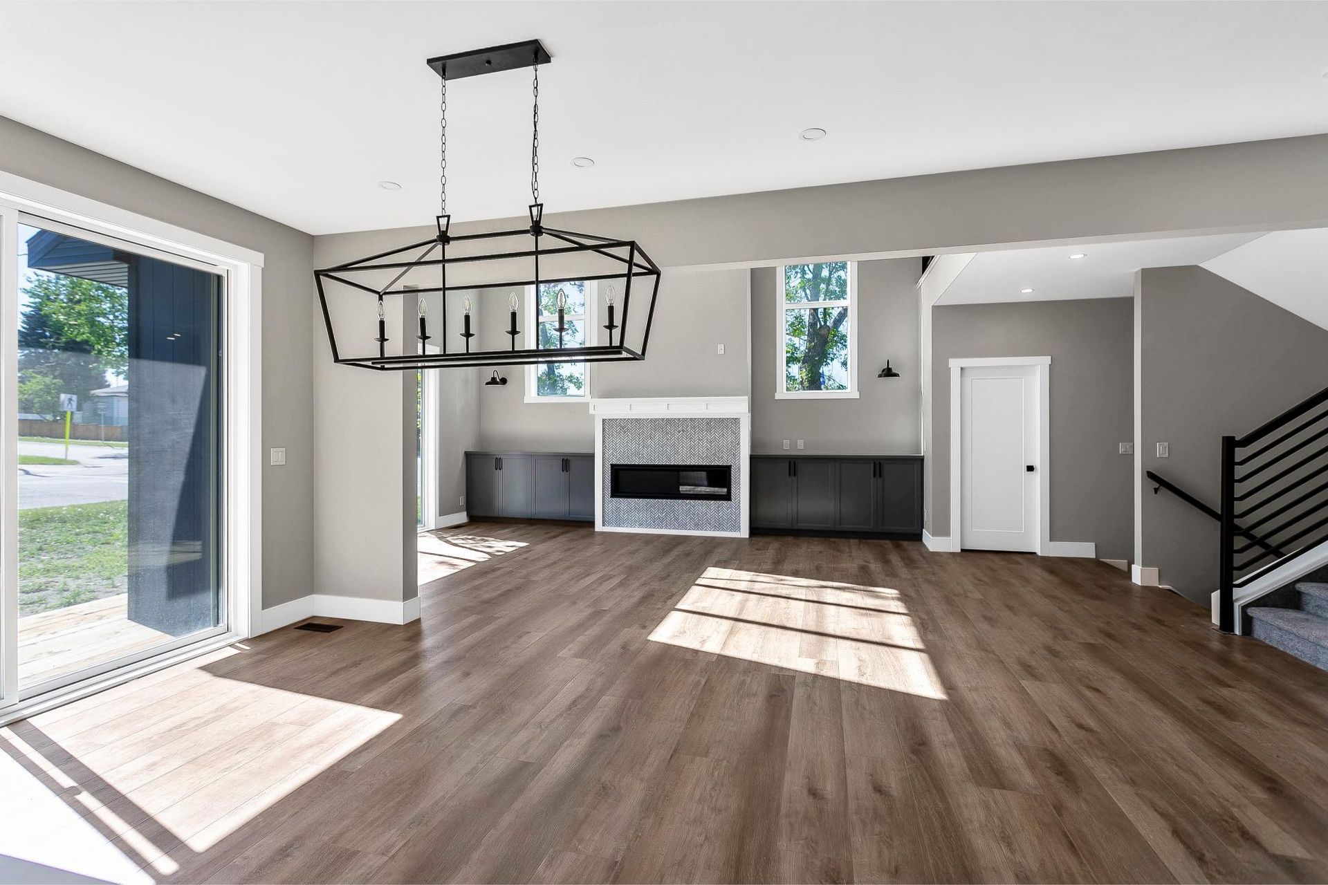 An open-concept living area with wood floors, grey walls, a modern chandelier, and a fireplace with built-in cabinetry.