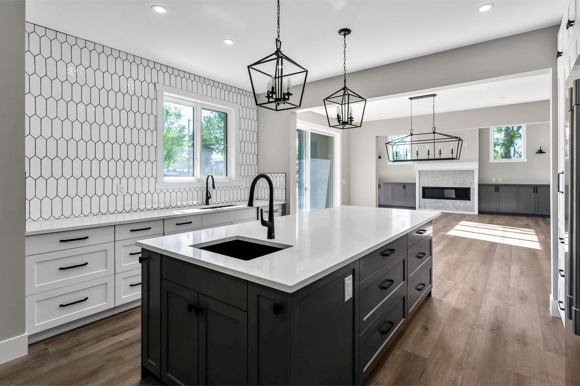 Modern kitchen with a dark gray island, white countertops, hexagonal backsplash tile, and pendant lighting.