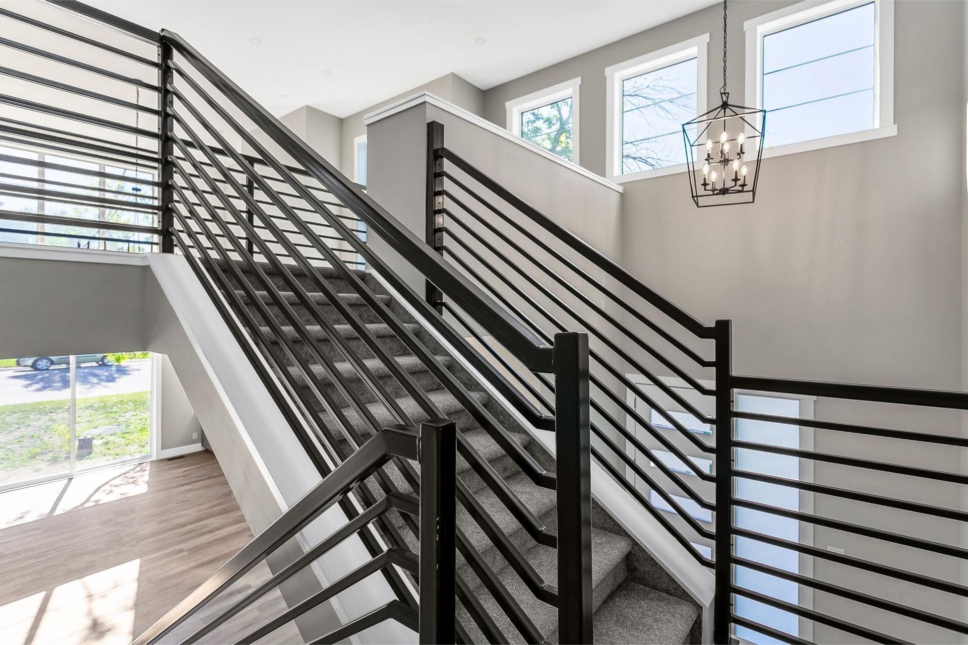 Modern staircase with black metal horizontal railings, gray carpeted steps, and a decorative pendant light fixture.