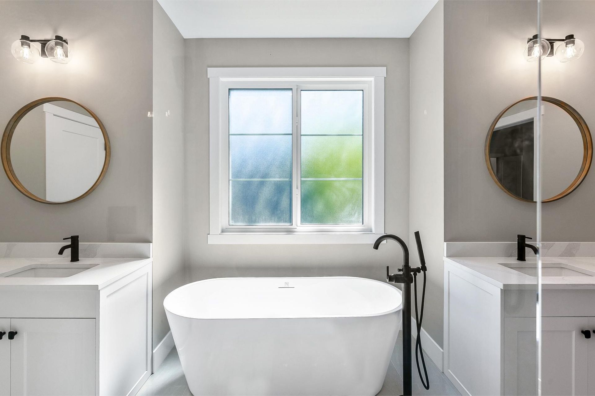 Modern bathroom featuring a central freestanding white tub, dual vanities with round mirrors, and matte black fixtures.