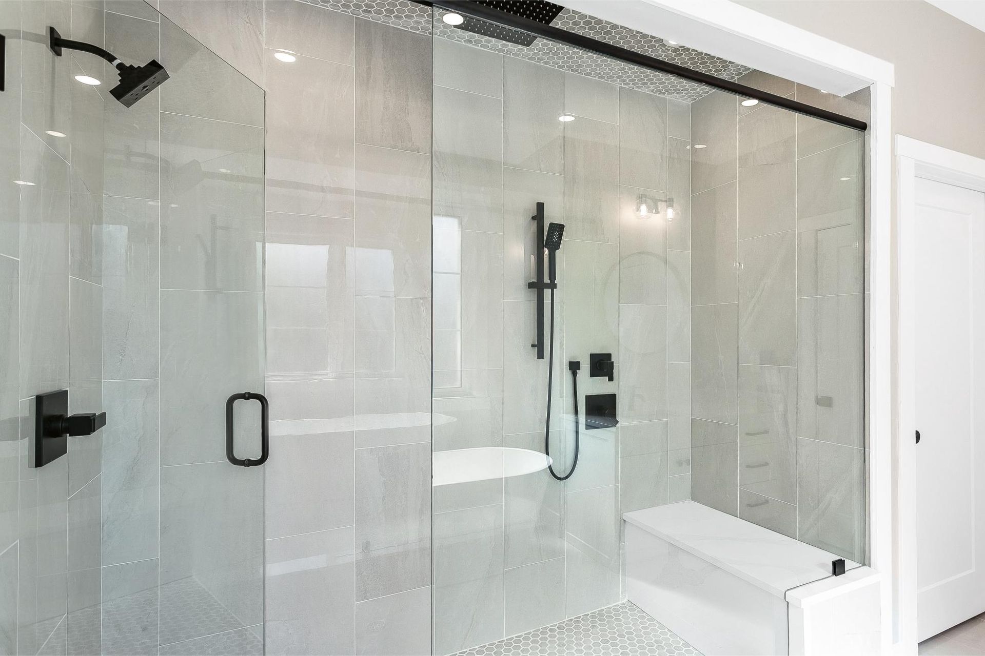 A modern glass walk-in shower with black fixtures, a handheld showerhead, and a built-in tiled bench.