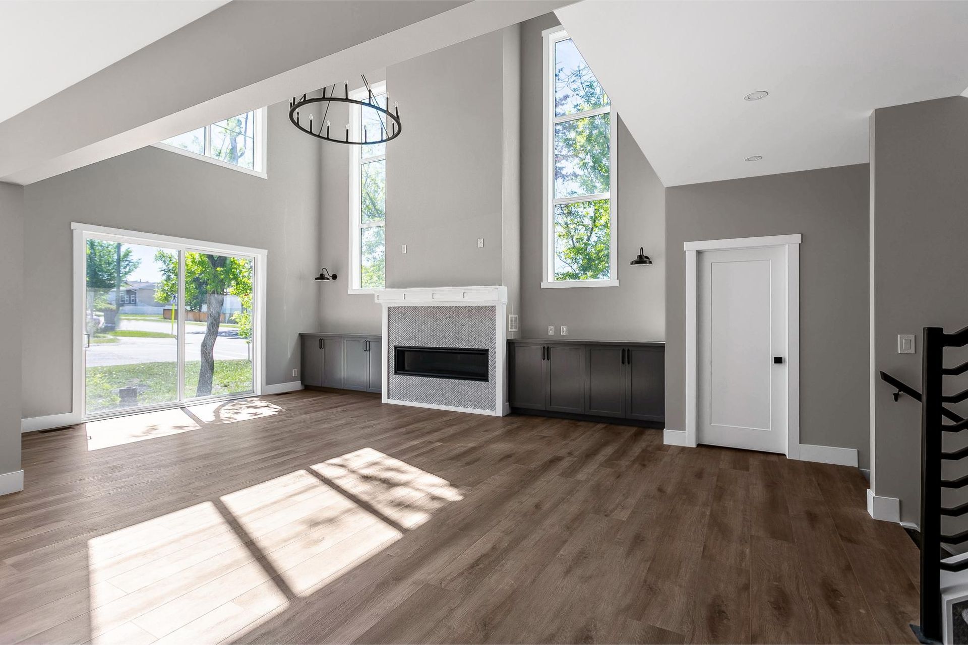 A sunlit living room with high ceilings, large windows, dark cabinetry, and a fireplace with a decorative tiled surround.