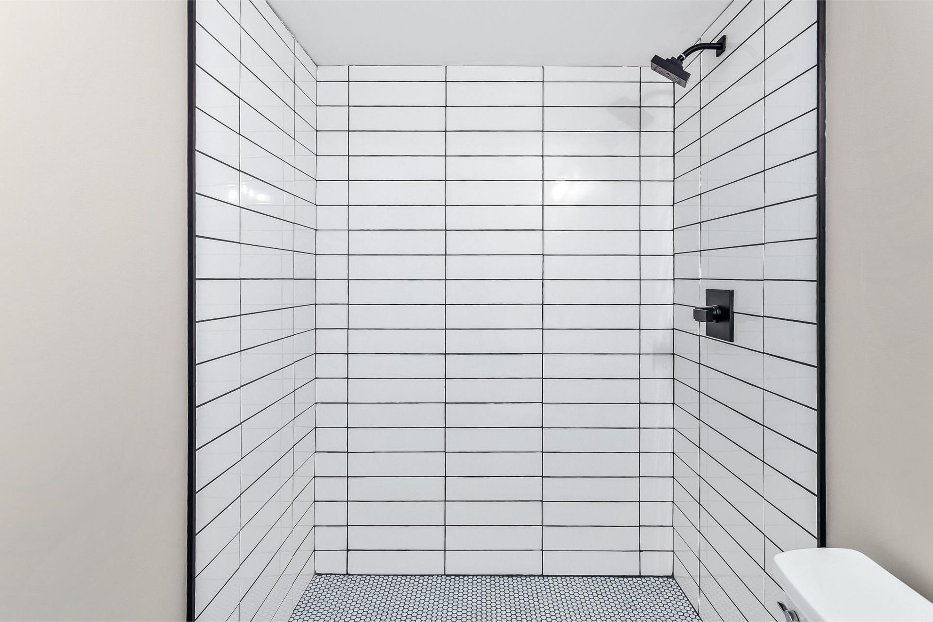 A shower with white subway tiles, black grout, black fixtures, and a patterned tiled floor.