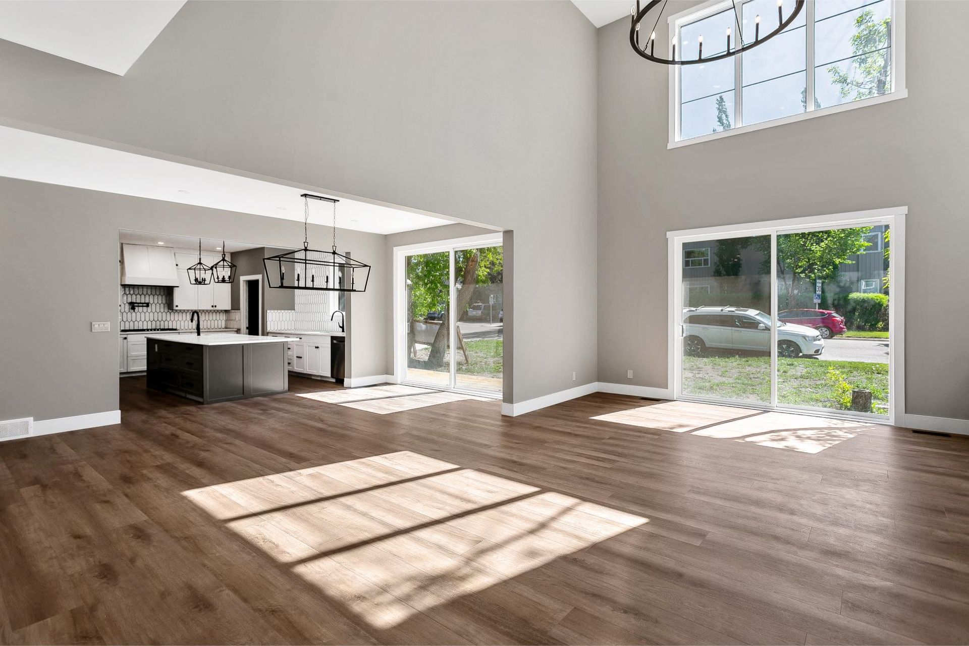 A spacious, modern open-concept living area with light grey walls, dark wood floors, and large sliding glass doors.