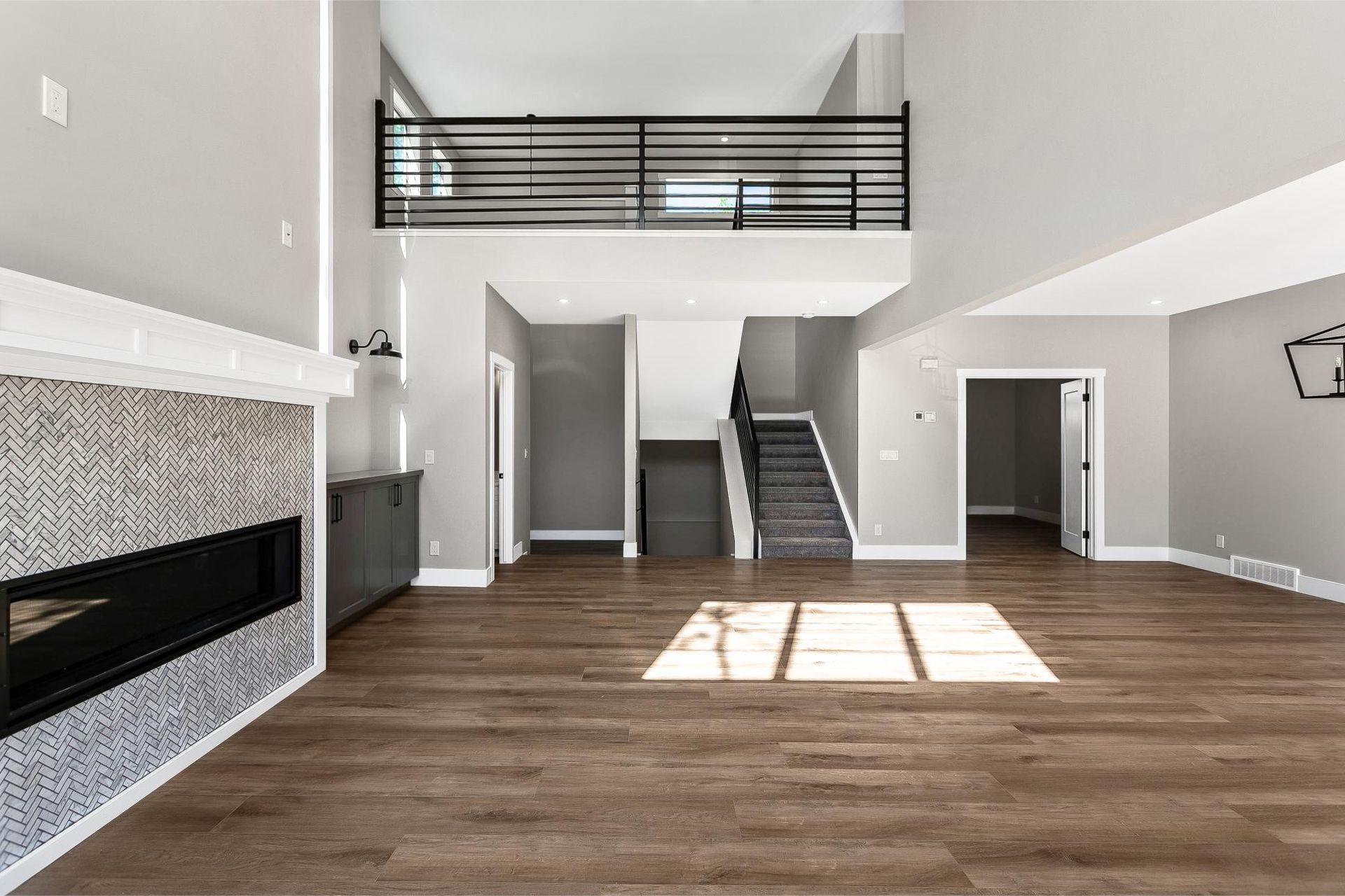 A spacious living room with wood floors, a tiled fireplace, and a balcony overlooking the area via a black metal railing.
