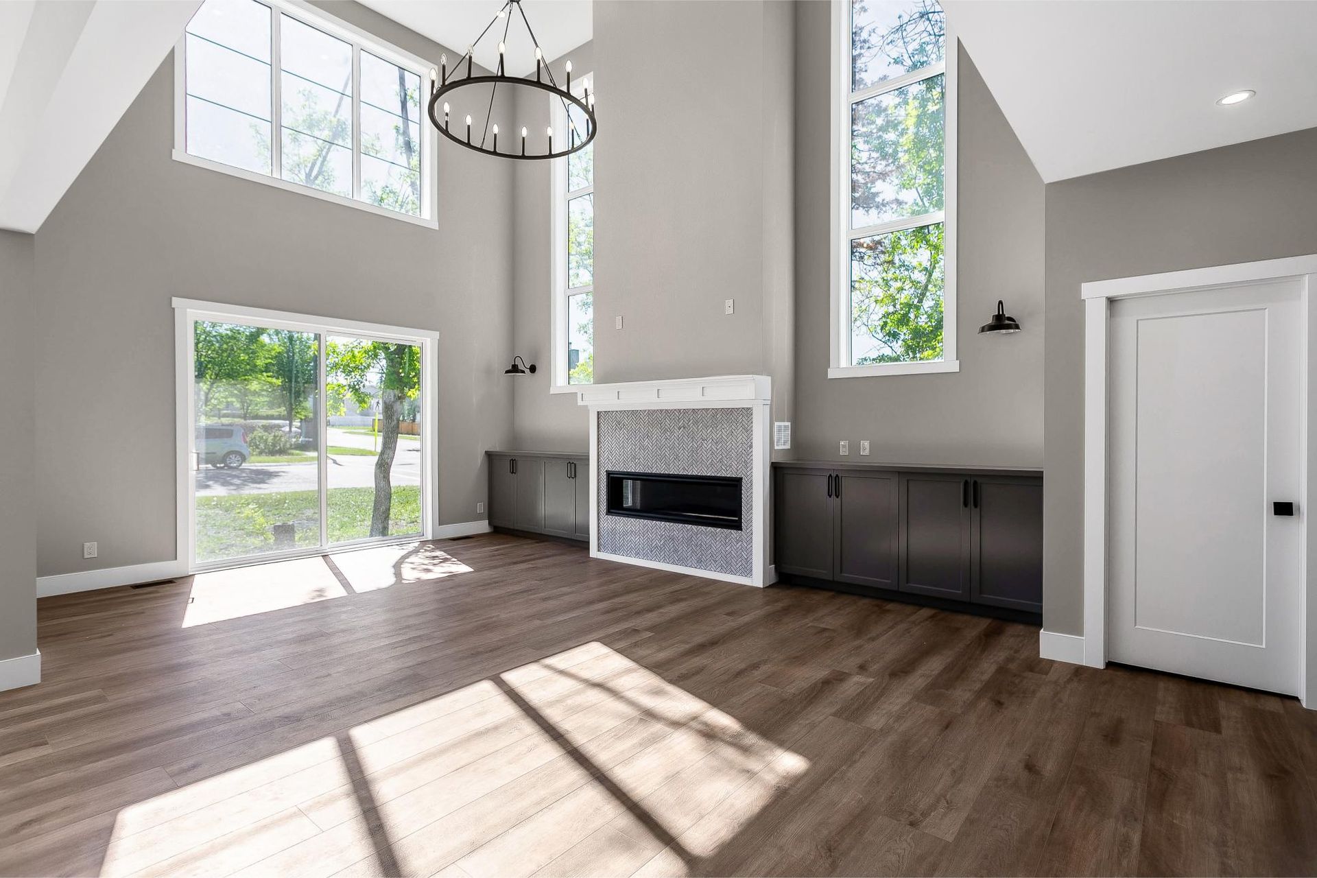 A bright living room with gray walls, wood floors, a modern fireplace with a tile surround, and tall windows.