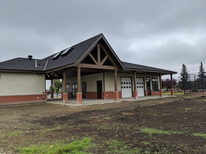 A one-story building with a brown wooden frame, brick base, cream siding, and a gabled roof set against a cloudy sky.