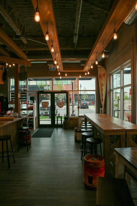 A rustic bar interior with wooden beams, pendant lighting, high tables, bar stools, and a view of the street through doors.