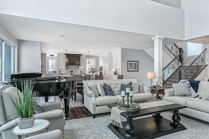 A spacious open-concept living room with white sofas, a black coffee table, a grand piano, and a staircase.
