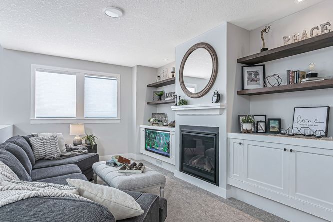 A cozy living room with a dark grey sectional, light grey ottoman, fireplace, and built-in shelving with decor.