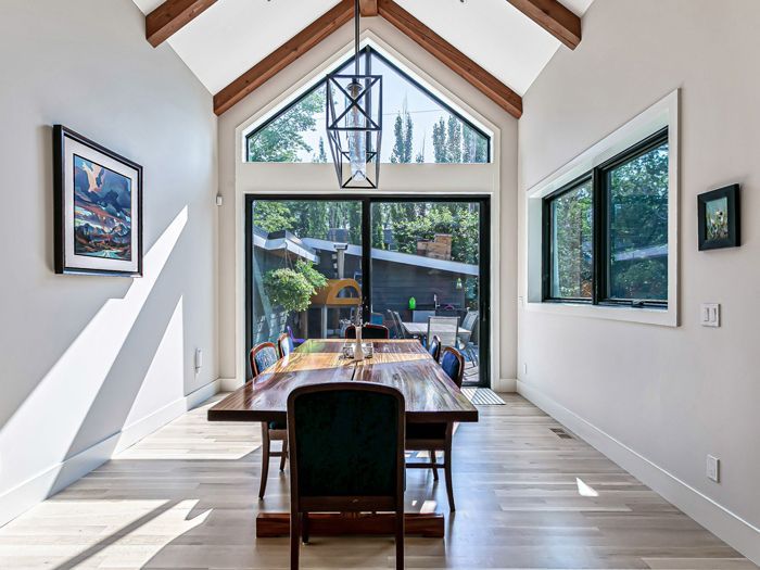 A dining room with a long wooden table, high vaulted ceilings, large windows, and a hanging pendant light.