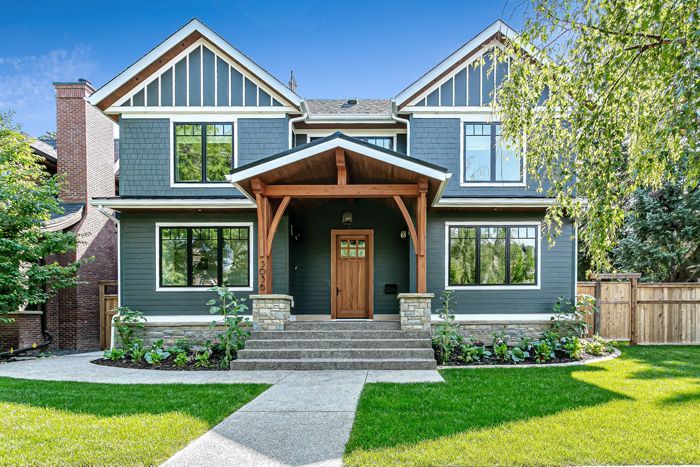 Two-story blue-gray home with dark-trimmed windows, a wooden front porch, stone base, and gabled roofline.