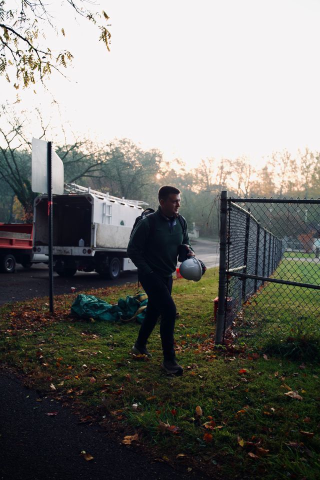 Person holding a soccer ball near a chain-link gate in a grassy yard at dusk.