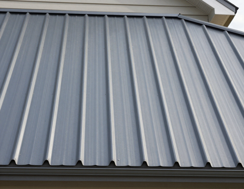 Gray corrugated metal roof on a house under a cloudy sky