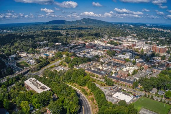 Aerial view of a suburban town with roads, trees, buildings, and distant hills under a blue sky