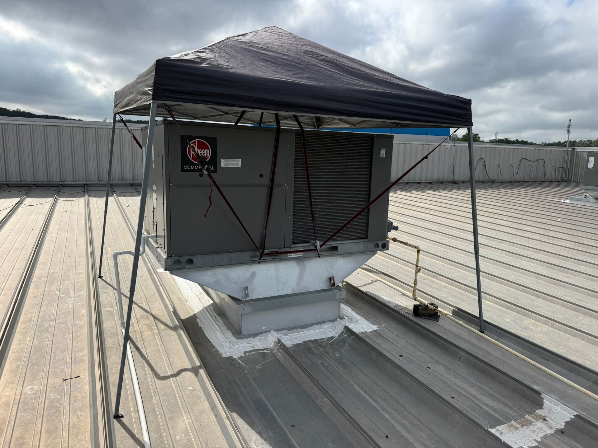 Rooftop HVAC unit under a black canopy, surrounded by concrete rooftop barriers.
