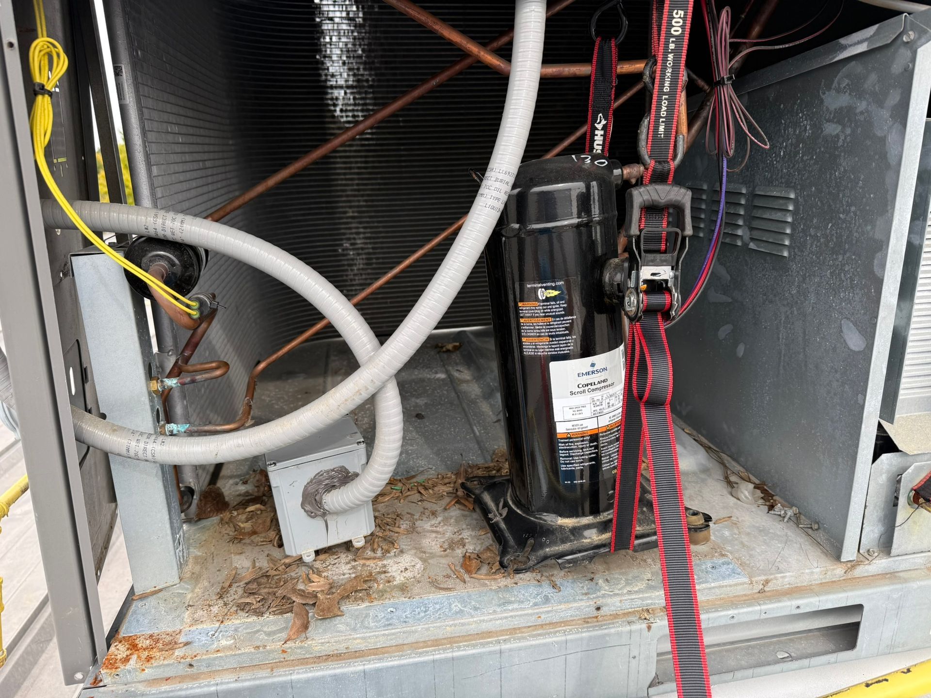 Open electrical panel with pipes and wires; a black pump/compressor sits inside beside dusty metal walls.