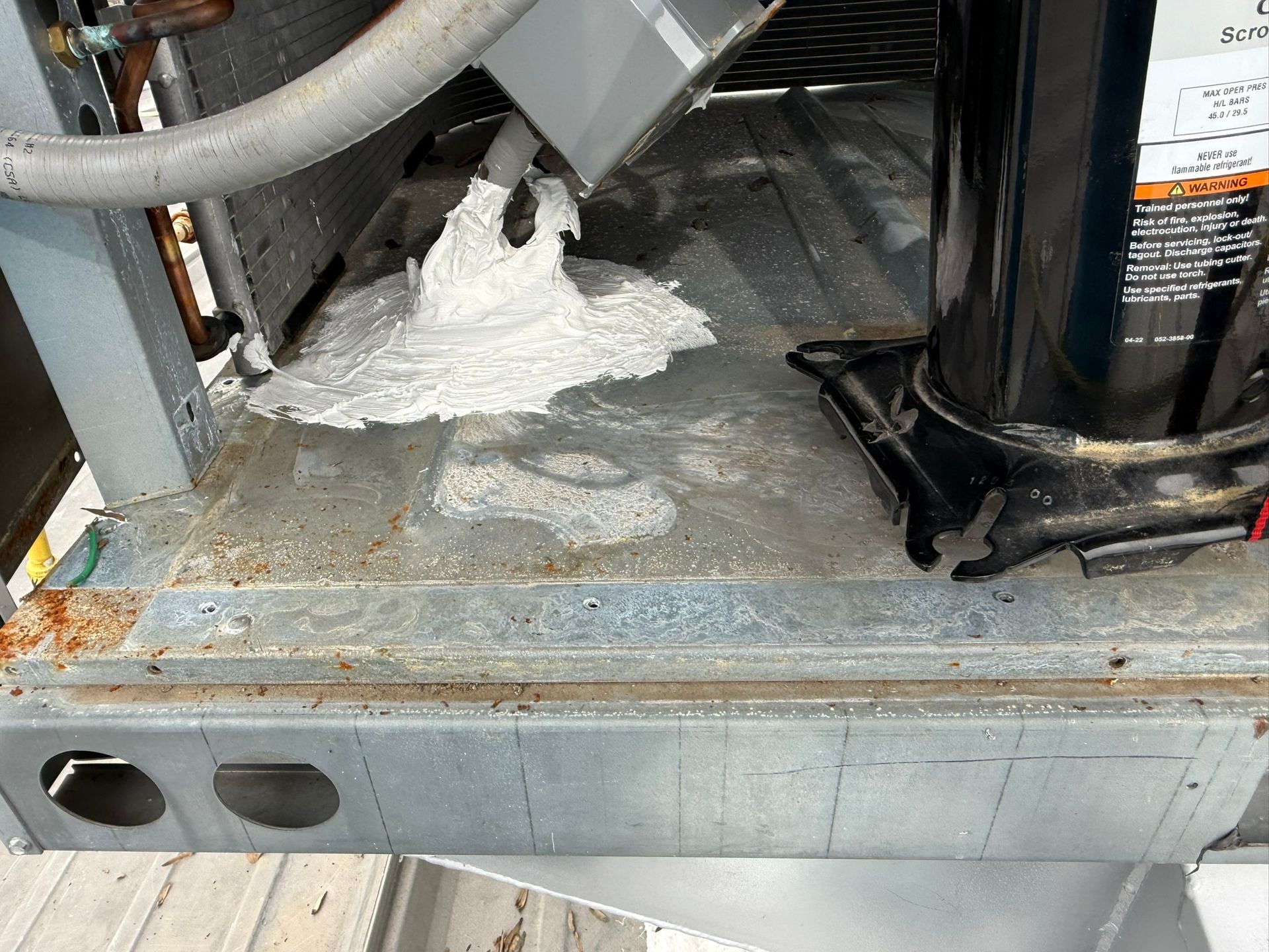 White powder spilled on a metal HVAC unit beside pipes and a black compressor.