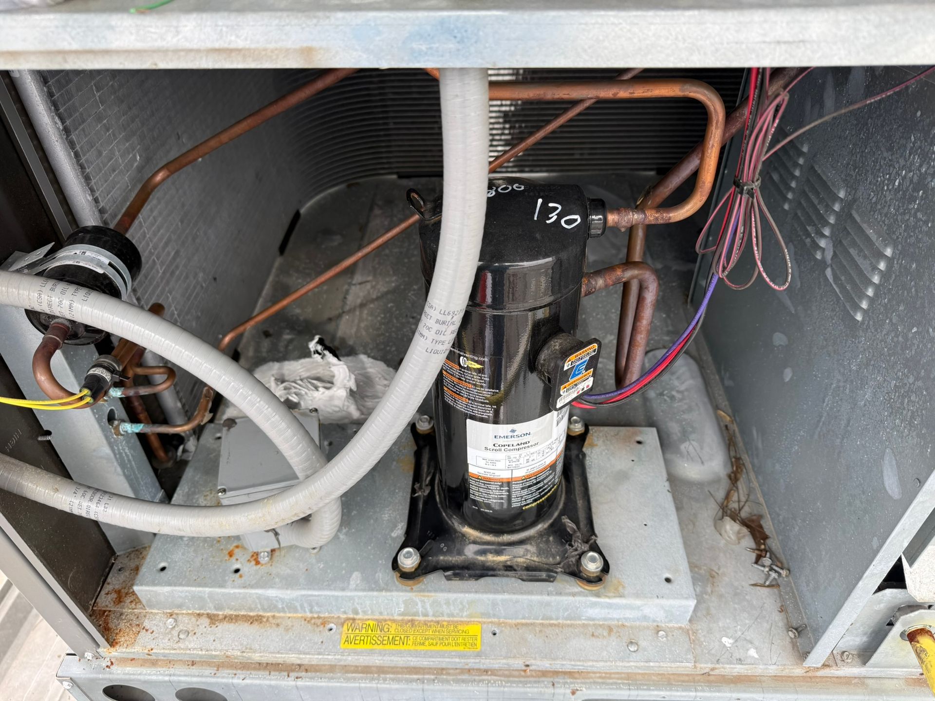 HVAC compressor compartment with copper tubing, wires, and rust-stained metal base at the bottom of an outdoor unit