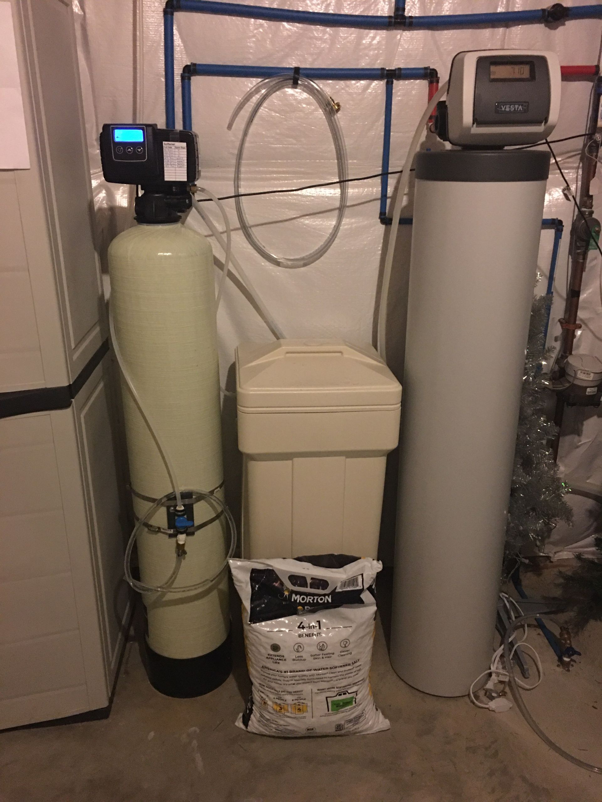 A water softener is sitting next to a water heater in a basement.